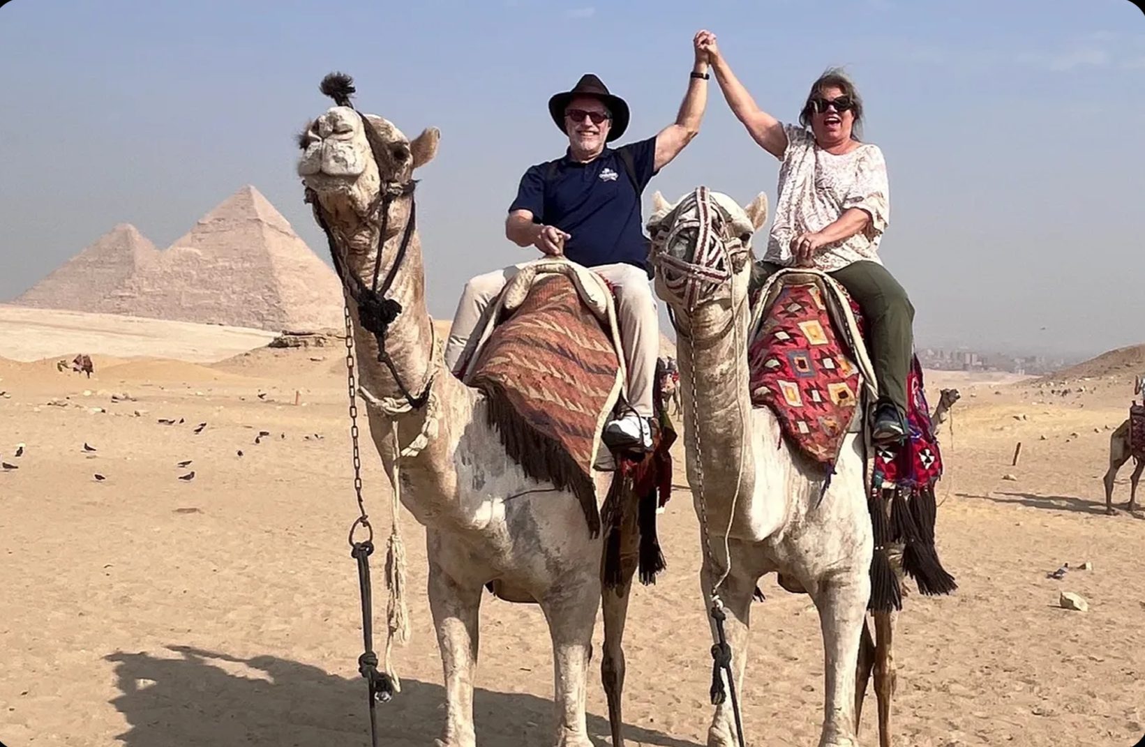 Two people on camels near pyramids
